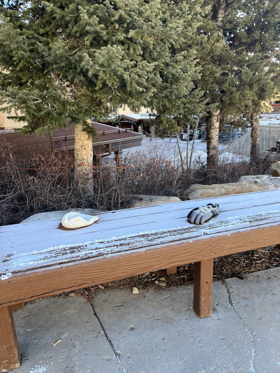 A beanie and a single ski glove left frozen on a bench at a ski resort base area
