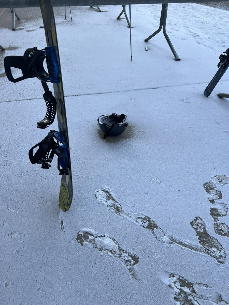 A kids ski helmet left upside down on a frosty walkway next to a snowboard