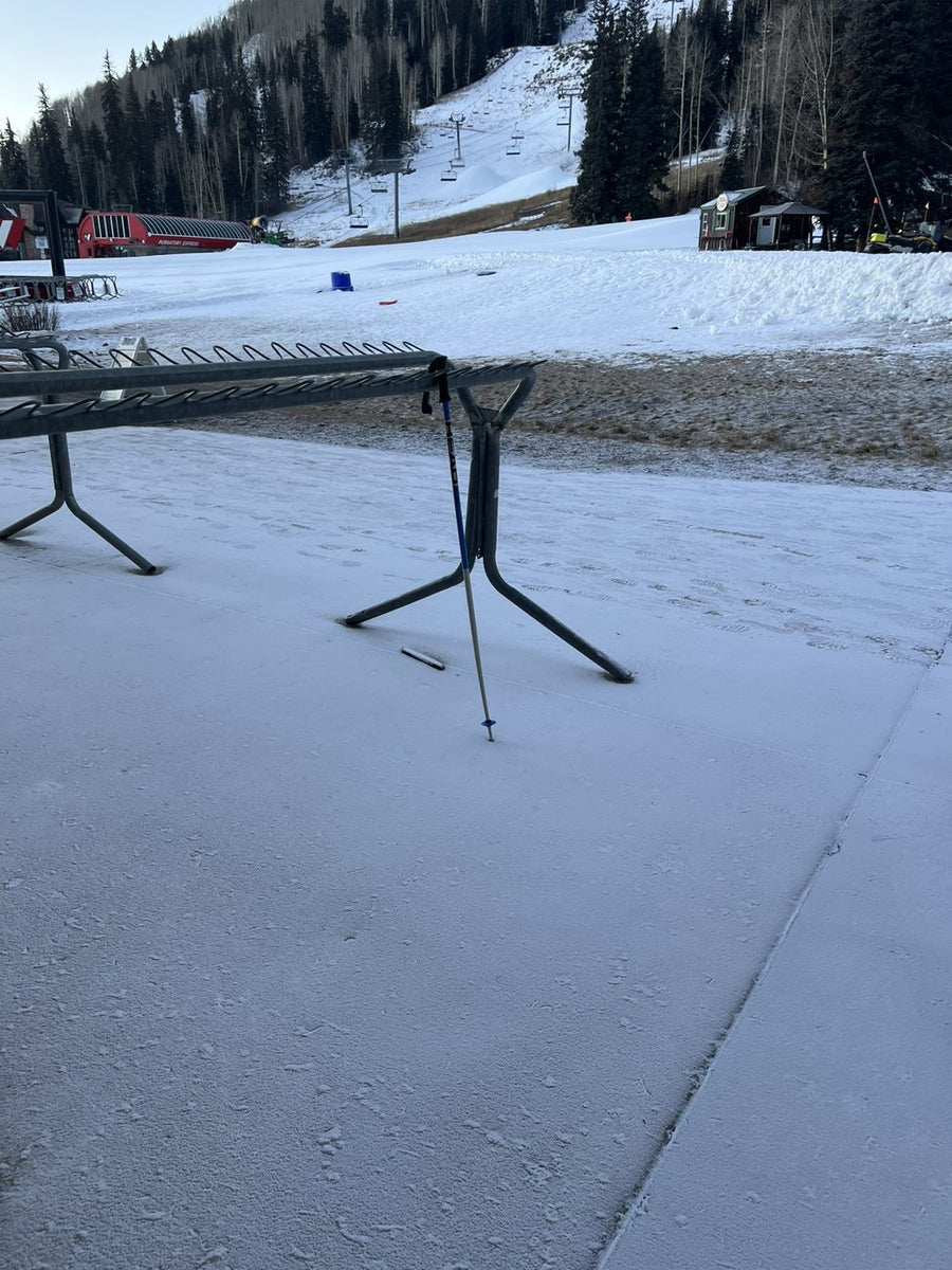A single ski pole left leaning against an empty ski rack at closing time